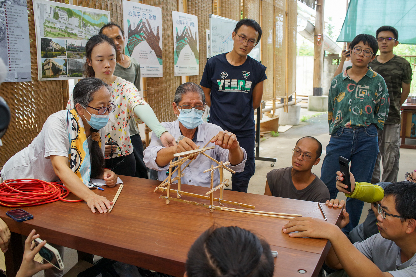 Maidang explique comment on place les Panubayon, pilotis obliques, dans la construction. Ils servent bien entendu à renforcer la structure mais ont aussi un sens symbolique. Puisqu’il faut en même temps des personnes qui travaillent en bas et en haut de la construction pour les placer, et parce qu’ils relient le sol au toit, ils représentent la cohésion du village. (© Sasa)