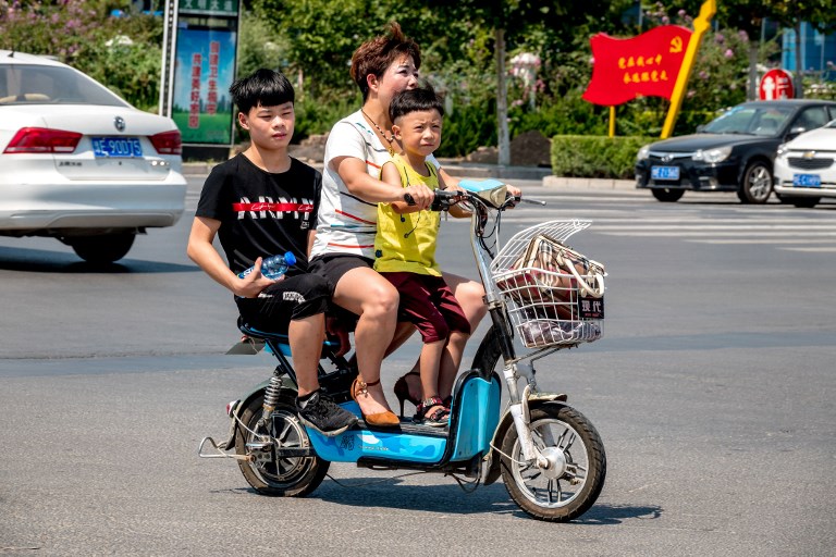 圖為中國河南滑縣一名婦女騎電動車帶著兩個孩子。示意圖。(AFP)