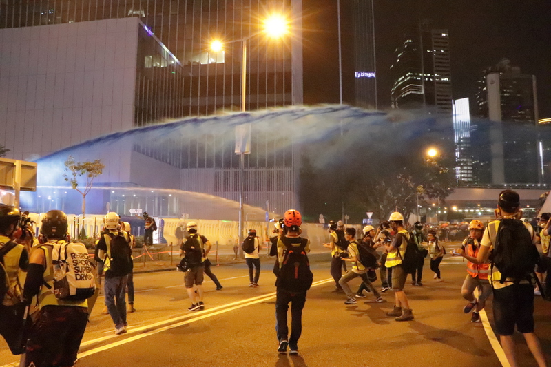 香港示威者28日晚間朝政府總部投擲汽油彈，港警於8時42分出動水炮車噴射藍色水柱及胡椒水。(中央社)
