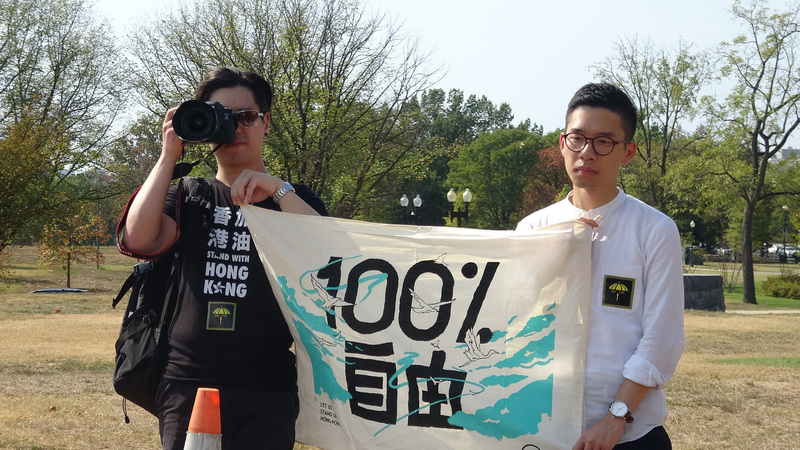 上百名港、台、美民眾28日聚集華府響應929全球撐香港活動。香港眾志常委羅冠聰（右）舉著「100%自由」旗幟說，這是致敬追求言論自由與台灣主權的「自由時代」創辦人鄭南榕。(圖：中央社)