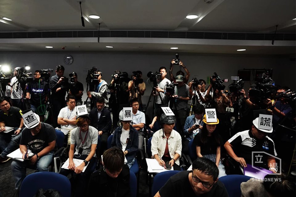 香港警方4日下午就最近反送中示威事件召開記者會，現場坐著6位記者，頭上戴著貼有「查警暴、止警謊」等標語的頭盔。(圖： Stand News立場新聞提供)