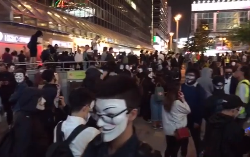 港民5日晚間發起「全民V煞日」(V煞台灣稱為V怪客)，一批市民晚間身穿黑衣及戴上V怪客面具，在尖沙咀市政局百周年紀念花園聚集。(圖擷自YouTube)