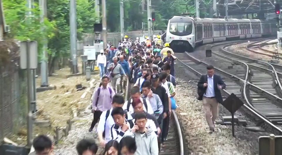 有示威者向沙田站路軌扔雜物，列車暫停，大批乘客需下車步往月台。  （圖片來源：有線新聞直播截圖）