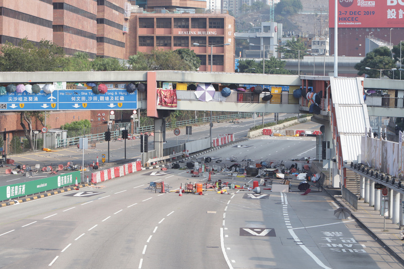 示威者從橋上向海底隧道路面投下雜物，令道路阻塞。圖為示威者站在連接理工大學的橋上，用雨傘遮擋自己。(圖：中央社)