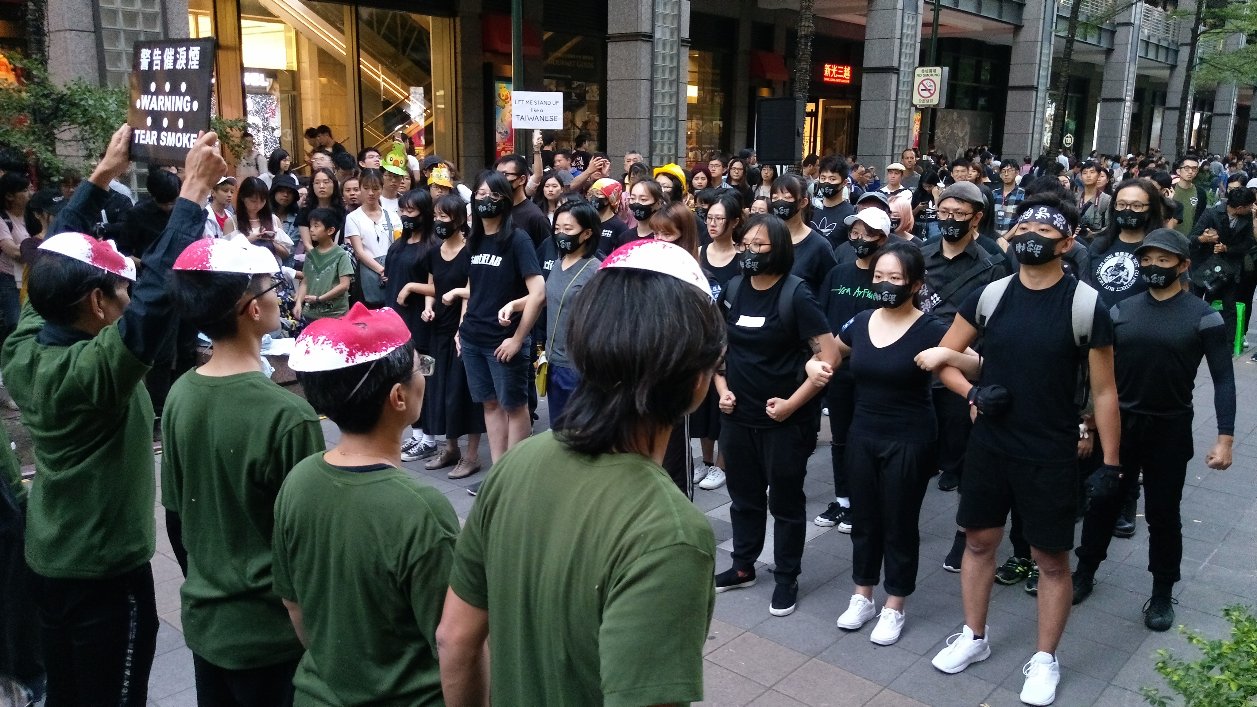 舉起「警告催淚煙」的告示牌，台北信義區街頭上演一群港警與反送中青年對峙的場面。(陳國維 攝)