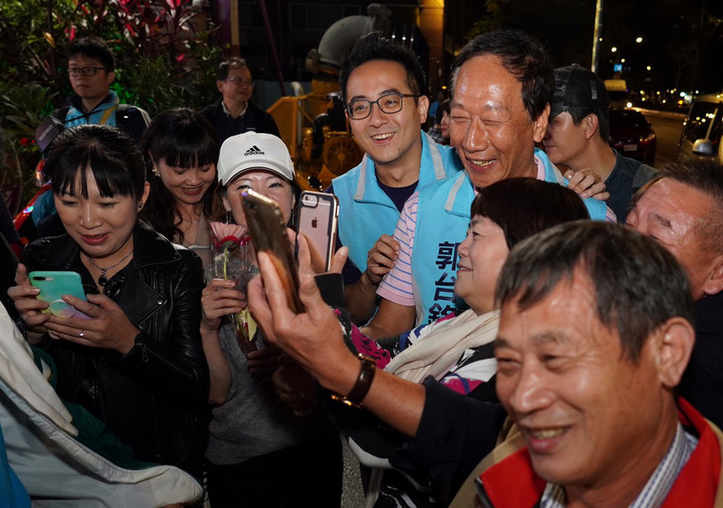 鴻海集團創辦人郭台銘（藍色背心右）22日晚間陪新北市立委第10選區參選人李縉穎（藍色背心左）掃街拜票，受到民眾歡迎，爭相上前要求合影。（李縉穎競選辦公室提供）