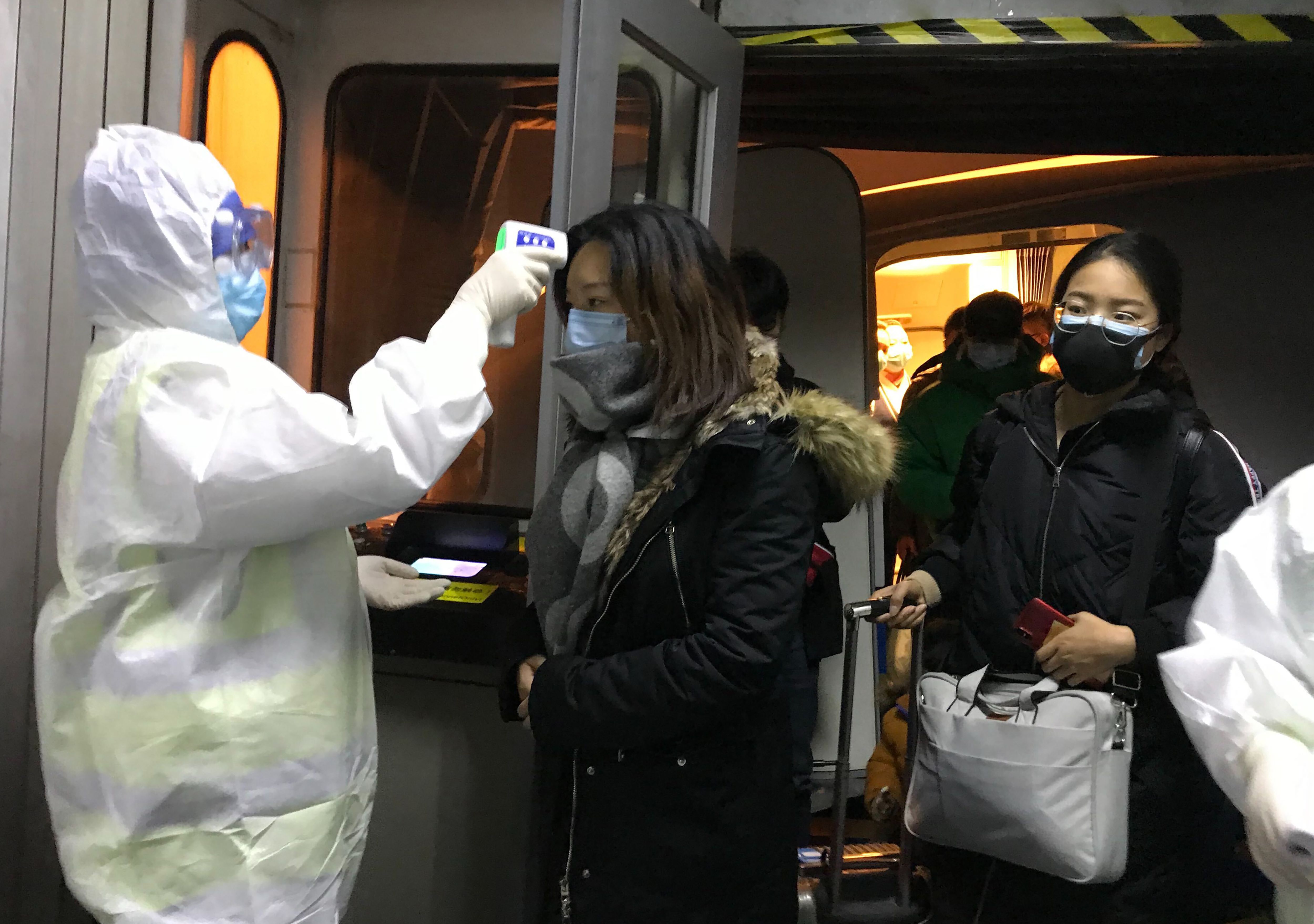 武漢肺炎疫情迅速蔓延。圖為北京機場身穿隔離衣的檢疫人員，對來自武漢班機的民眾進行體溫量測。(美聯社/達志影像)