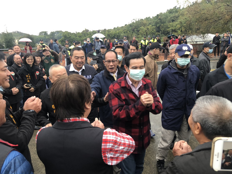 前總統馬英九（前中）26日年初二前往苗栗縣通霄鎮馬家庄祭祖，雖然下著雨，仍吸引近百名鄉親排隊領取福卡；因應武漢肺炎疫情，馬英九全程戴口罩、拱手不握手向民眾拜年。(圖：中央社)