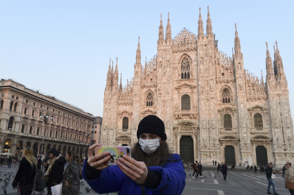 圖為一名戴口罩女子在米蘭的主教座堂廣場(Piazza del Duomo)前自拍。(AFP)