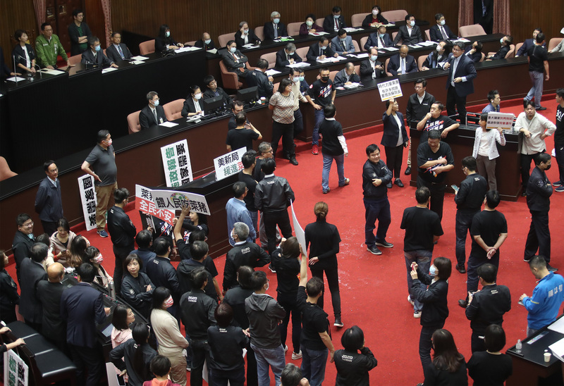 行政院長蘇貞昌27日第13度赴立法院進行施政報告並備質詢，時代力量邱顯智（拿麥克風者）質詢時，受到國民黨立委拿紙板阻擋與哨音干擾，便站到椅子上發言。(圖：中央社 )