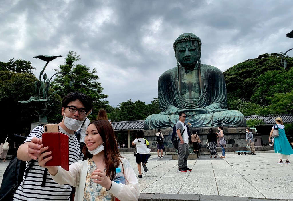 圖為1對遊客今年6月間在日本神奈川縣鎌倉市高德院的鎌倉大佛前拍照留念。 (AFP)
