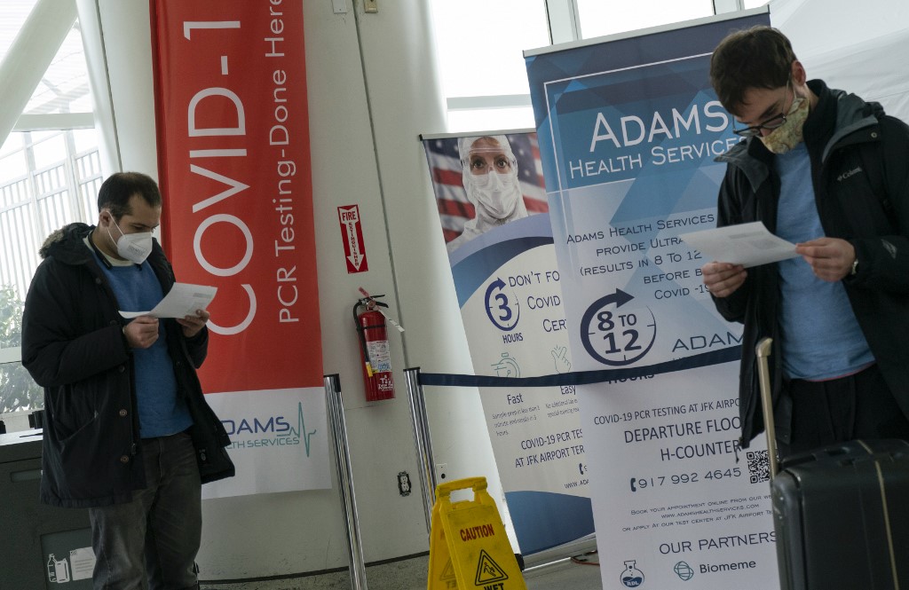 圖為美國紐約甘迺迪機場的旅客在看COVID-19檢測結果。 (AFP)