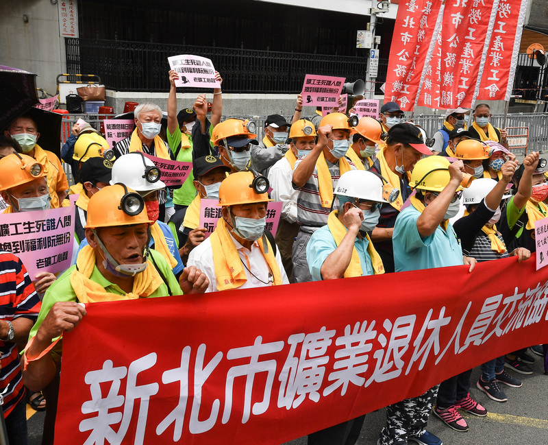 一群老礦工1日在勞工大遊行前戴起頭燈，先在立法院群賢樓前集結，高舉標語、喊口號，要求政府聆聽他們的訴求，也呼籲政府積極照顧老礦工的老年生活。 (圖：中央社)