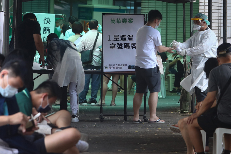 疫情升溫，台北市萬華區快篩站持續有民眾前往篩檢，醫護人員落實消毒防疫工作。 (圖：中央社)