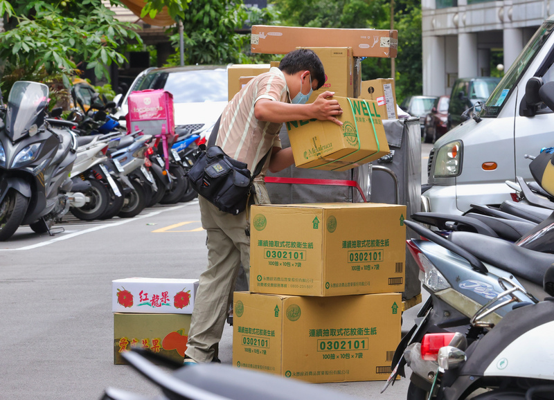 國內COVID-19疫情嚴峻，民眾減少出門，在家使用網路購物，導致包裹數量大增，宅配業者工作量也增加。圖為快遞員8日在街頭忙著整理包裹。 (圖：中央社)
