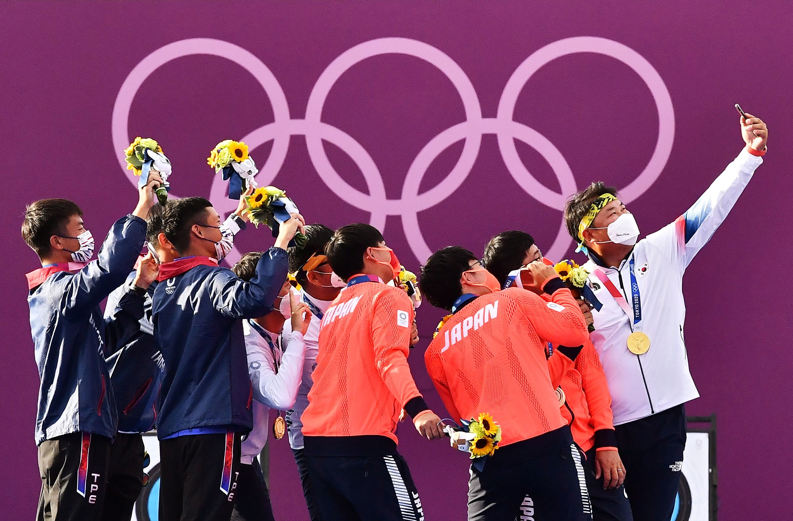 東京奧運26日射箭男子團體對抗賽，金銀銅牌分別由韓國（白衣）、台灣（藍衣）及日本（橘衣）拿下。頒獎典禮後，韓國隊提議3隊選手一起自拍留念。（路透社/達志影像）