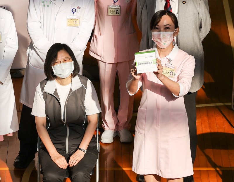 國產高端疫苗23日開始施打，總統蔡英文（左）一早前往台大醫學院體育館，依照相關流程，報到、醫師問診、接種疫苗。圖為蔡總統在施打前請護理師舉起國產高端疫苗外盒，讓眾人觀看。 (圖：中央社)