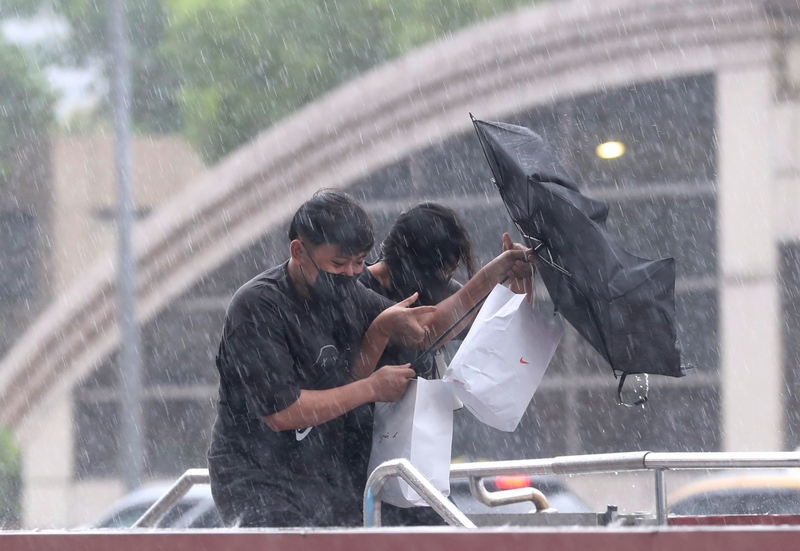 颱風璨樹來襲，台北市12日午後雨勢明顯，民眾出門撐傘避雨，但雨傘仍被強風吹到變形。 (圖：中央社)