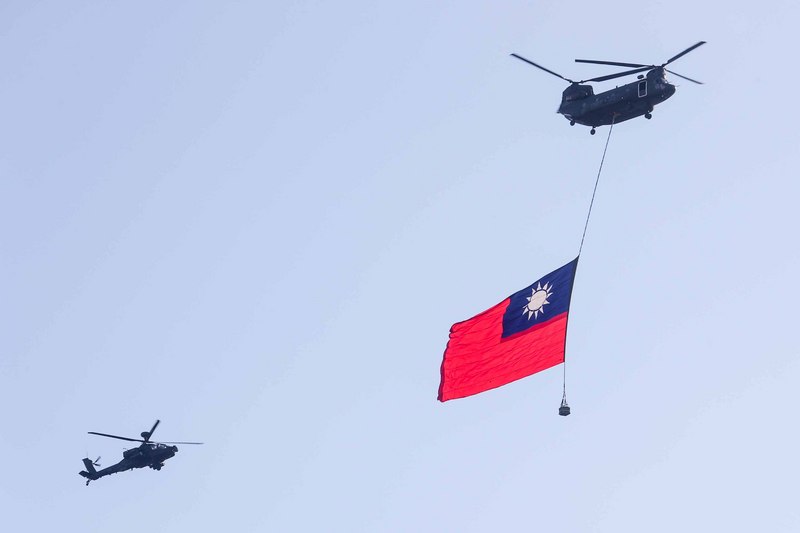 國軍30日舉行空中全兵力預演，空軍CH-47運輸直升機吊掛巨幅國旗，在AH-64E阿帕契直升機伴飛下通過台北上空。 (圖：中央社)