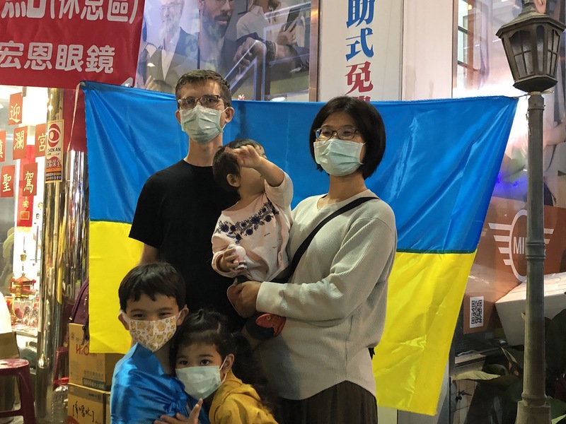 台中大甲鎮瀾宮媽祖鑾轎16日凌晨從彰化市出發前往台中市，彰化市有1處大甲媽補給站攤位，懸掛烏克蘭國旗，擔任補給站攤位志工的是老家在烏克蘭基輔市的車迪瑪（後左）和妻子林香君（後右），車迪瑪夫妻也向媽祖祈求和平，讓他們早日取得合法夫妻身分。（民眾提供） (圖：中央社)