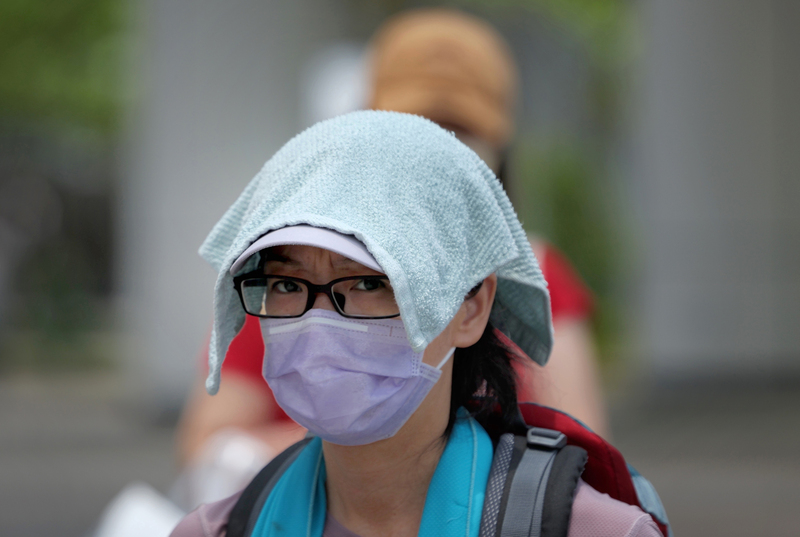 中央氣象局10日更新高溫資訊，雙北、南部等12縣市防36度高溫。圖為民眾中午在台北市南港區街頭，將布巾放在頭上遮陽。 (圖：中央社)