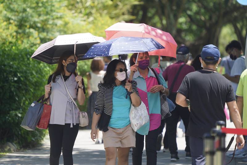 中央流行疫情指揮中心宣布，7日新增2萬1771例COVID-19（2019冠狀病毒疾病）本土病例，確診個案增中重症87例，其中42人死亡。圖為民眾在大安森林公園撐傘遮艷陽。 (圖：中央社)