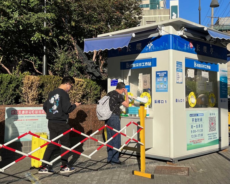 圖為上海市一處核酸檢測採樣亭，民眾排隊等待受檢。(圖：中央社)