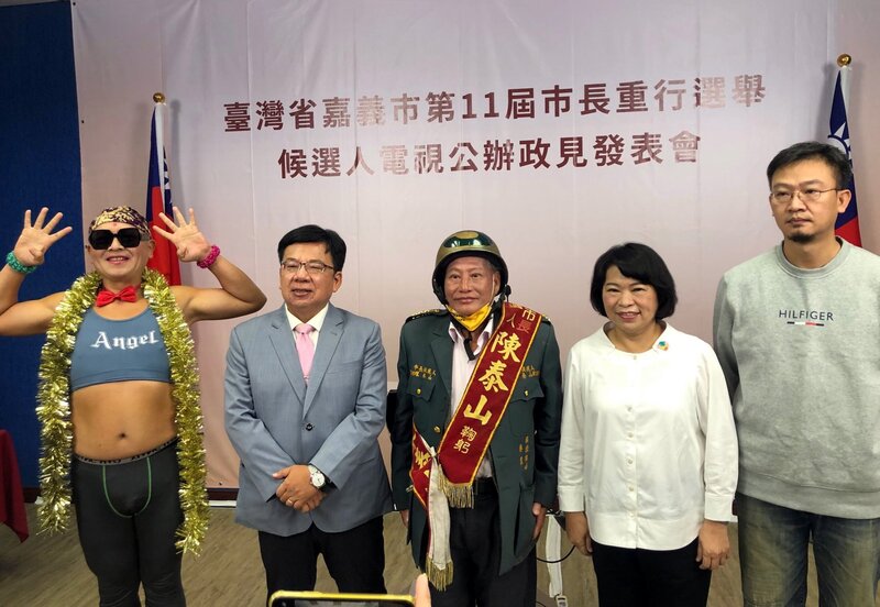 嘉義市選委會10日舉辦市長候選人電視公辦政見發表會，無黨籍鄭凱升（右起）、國民黨籍黃敏惠、無黨籍陳泰山、民進黨籍李俊俋、無黨籍黃宏成台灣阿成世界偉人財神總統出席合影。 (圖：中央社)