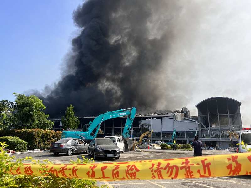 屏東科技產業園區明揚國際科技公司廠房22日發生火警，23日清晨現場仍冒出大量濃煙，大型機具進場清理廠房。 (圖：中央社)