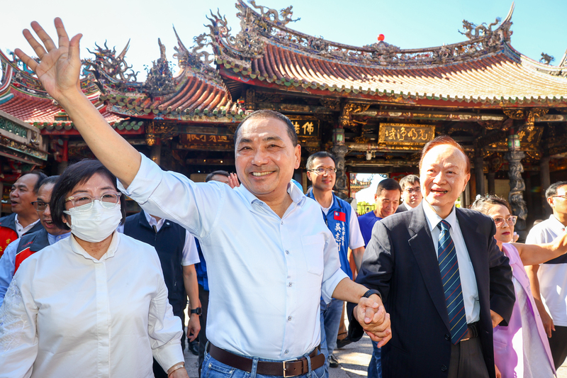 國民黨總統參選人侯友宜（前中）25日到艋舺龍山寺參拜，由龍山寺董事長黃書瑋（前右）親自接待，侯友宜向現場民眾揮手問好。 (圖：中央社)