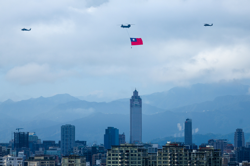 國慶將至，國軍28日展開空中全兵力預演，一架CH-47SD契努克運輸直升機（中）吊掛國旗飛越台北市上空。 (圖：中央社)
