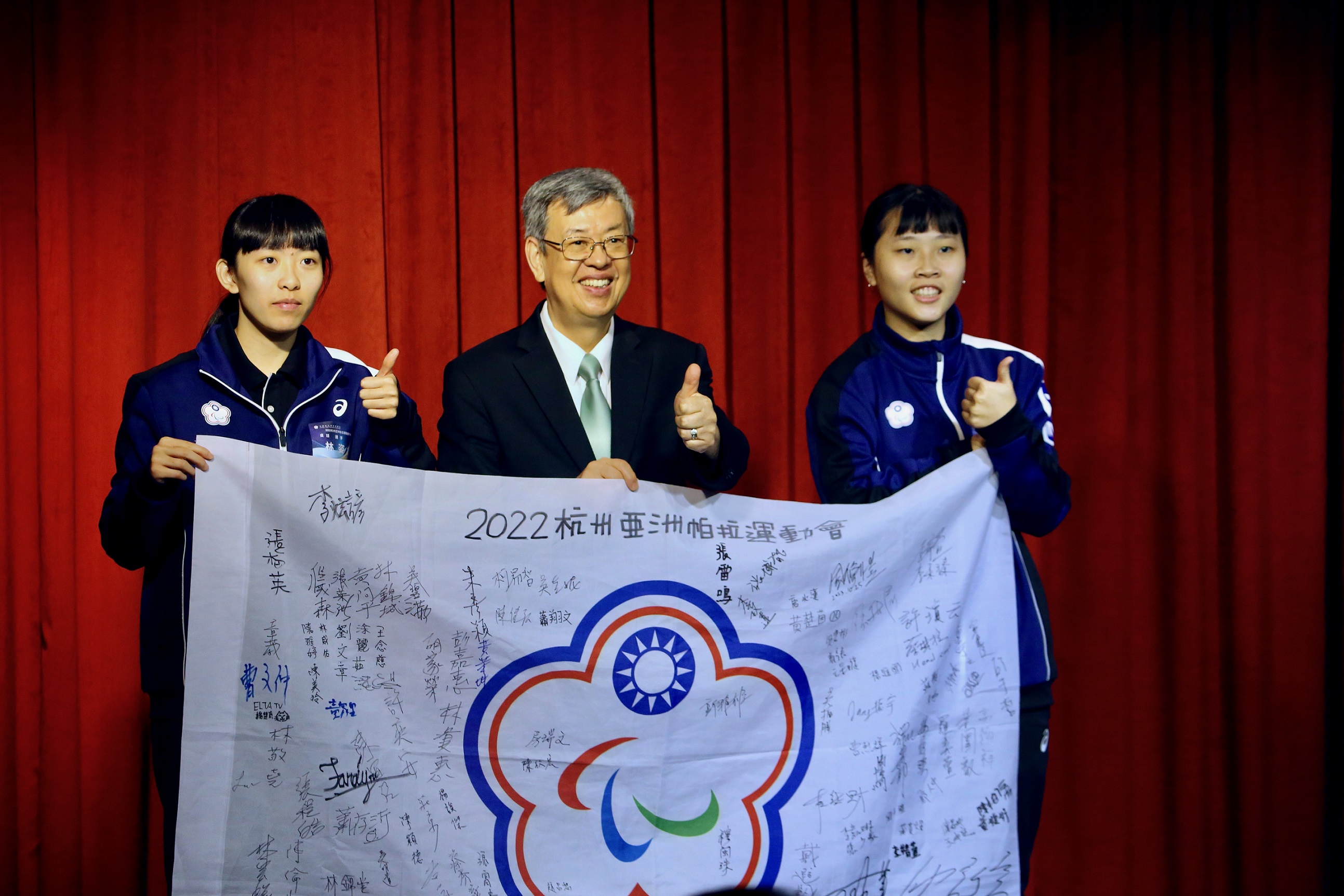 行政院長陳建仁設宴迎接亞帕運代表團榮耀歸國。圖為桌球選手林姿妤(左）及田曉雯(右)致贈陳建仁(中)亞帕運代表團簽名會旗。(體育署提供)