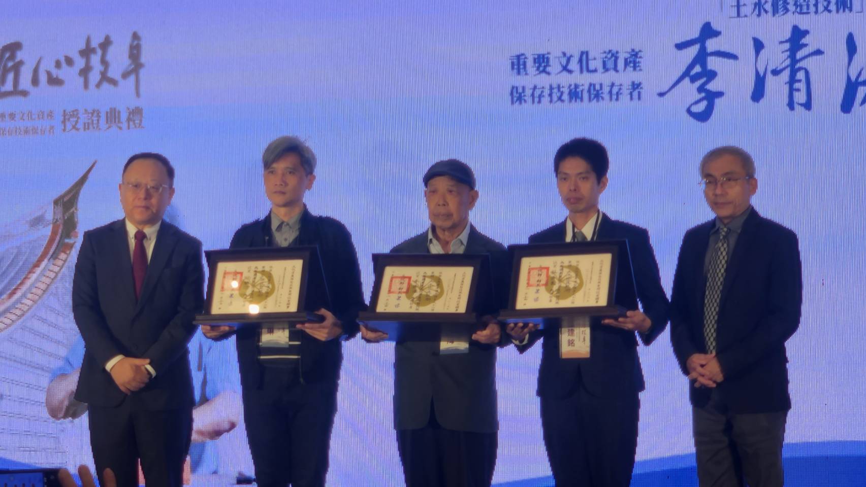 文化部長史哲(左一)24日親自授證「112年文化資產保存技術保存者」三位得主，由於蘇清良及徐明河兩位司阜今年相繼辭世，由蘇清良的孫子蘇建銘(右二)、徐明河的兒子徐朝琳(左二)代表接下證書，李清海(右三)則親自出席領獎。右為文資局長陳濟民。(江昭倫 攝)