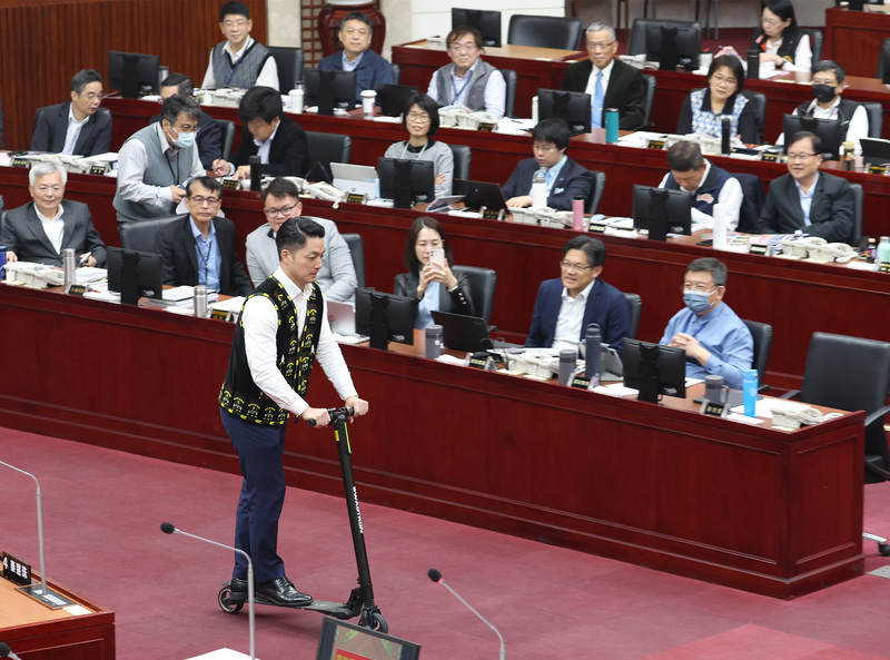 台北市長蔣萬安（前）30日接受市政總質詢，並在議場首度試騎電動滑板車，豈料差點撞上一旁桌子，他表示，電動滑板車速度快，上路其實很危險，但實際上仍有許多民眾違規，將依法加強取締。中央社記者張新偉攝  112年11月30日 (圖：中央社)