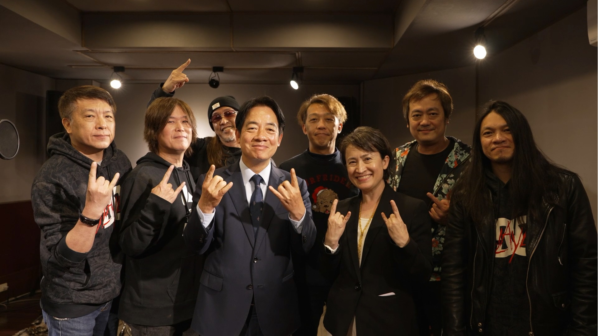 賴清德(前排左三)與蕭美琴(前排右二)與董事長樂團特地模仿「Rocker」手勢向國人拜年。(民進黨提供)