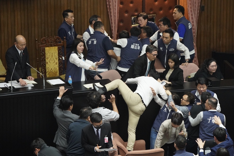 立法院會17日處理藍白所提國會改革法案，在處理報告事項逕付二讀、進行表決時，民進黨立委欲攻上主席台，朝野再度爆發推擠。圖為民進黨立委郭國文(卡其褲)試圖翻越突襲主席台，被國民黨立委攔下。(圖：中央社)