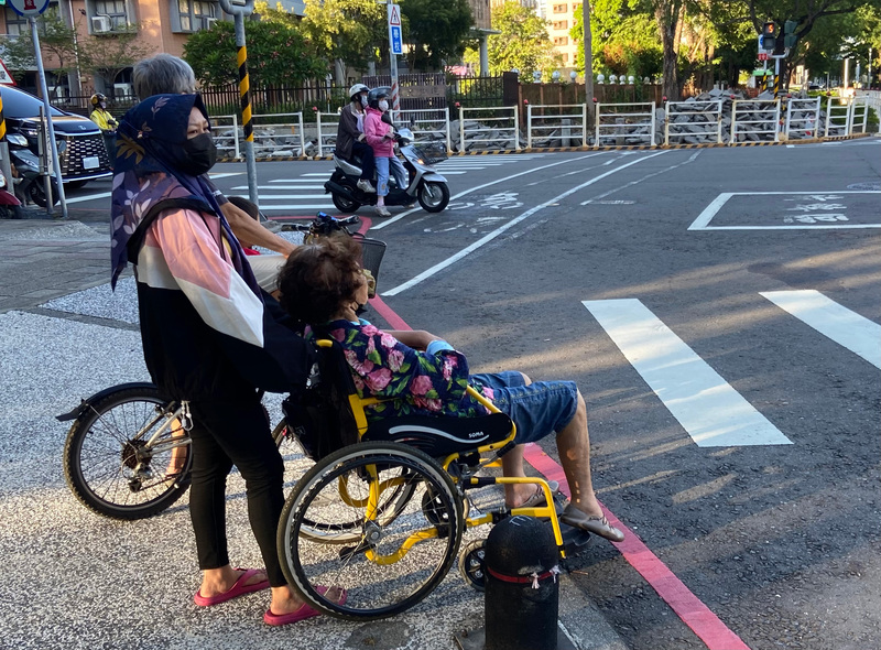 圖為家庭看護移工午後推著乘坐輪椅的長者前往公園散步。(圖：中央社)