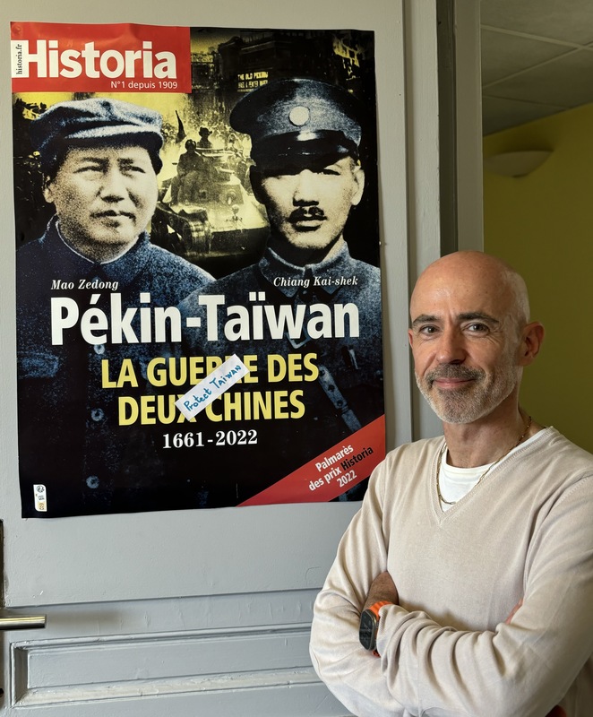 長期推動法國認識台灣的學者高格孚。後方海報為高格孚主編法國百年歷史雜誌Historia的台灣封面故事。 (圖：中央社)