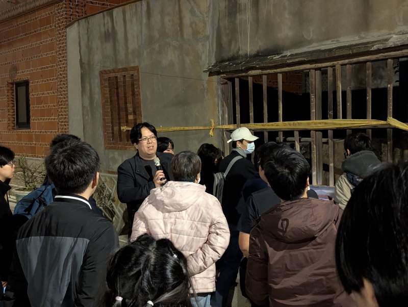 中山大學社會學系助理教授林傳凱（後左持麥克風者）20日在金門舉行講座，分享金門戒嚴時期政治案件研究成果，並帶領民眾走訪金城鎮南門境天后宮旁廢棄建築，原為1960年代後新生隊所在地。 (圖：中央社)