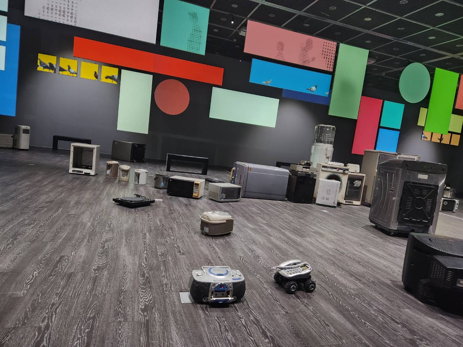 當代藝術館「No Language」展覽，將藝術家陳萬仁的錄像裝置《這不是一個幌子》和廖建忠利用廢棄生活家電改造的遙控車的作品《運転生活終點站3.0 K-US》放在同一空間展示，是對人類忙碌生活、消費文化的幽默調侃。(江昭倫 攝)