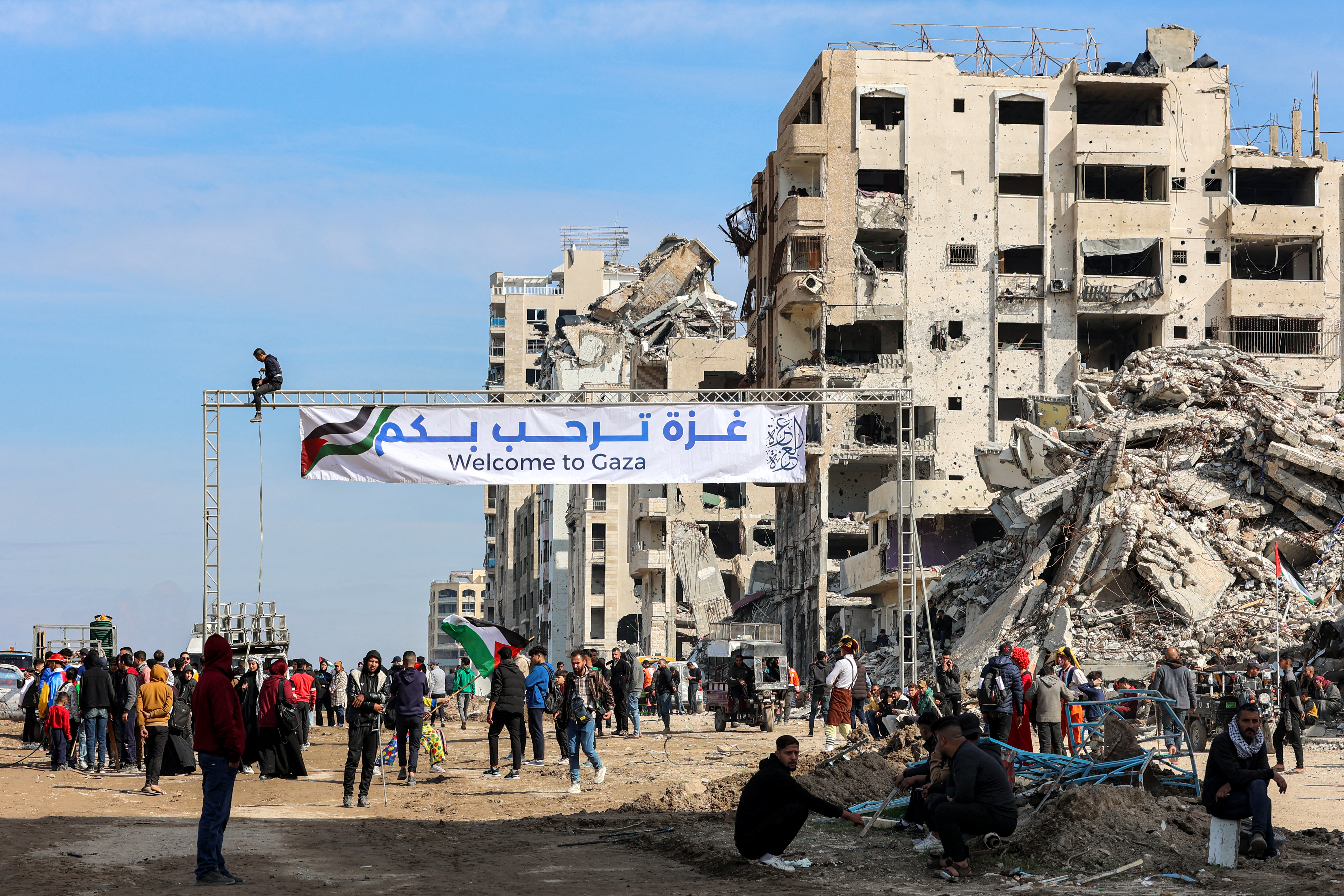 加薩民眾聚集在加薩沿海一棟倒塌建築廢墟附近並拉出標語，歡迎其他人從加薩走廊南部穿越進入加薩城。(AFP)