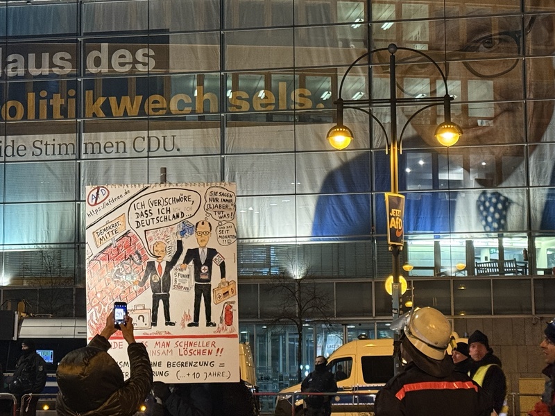 圖為德國柏林民眾9日在基民盟總部前高舉漫畫抗議看板，批評目前民調最高的總理候選人梅爾茨與極右翼另類選擇黨合作推動移民緊縮政策。(圖：中央社)