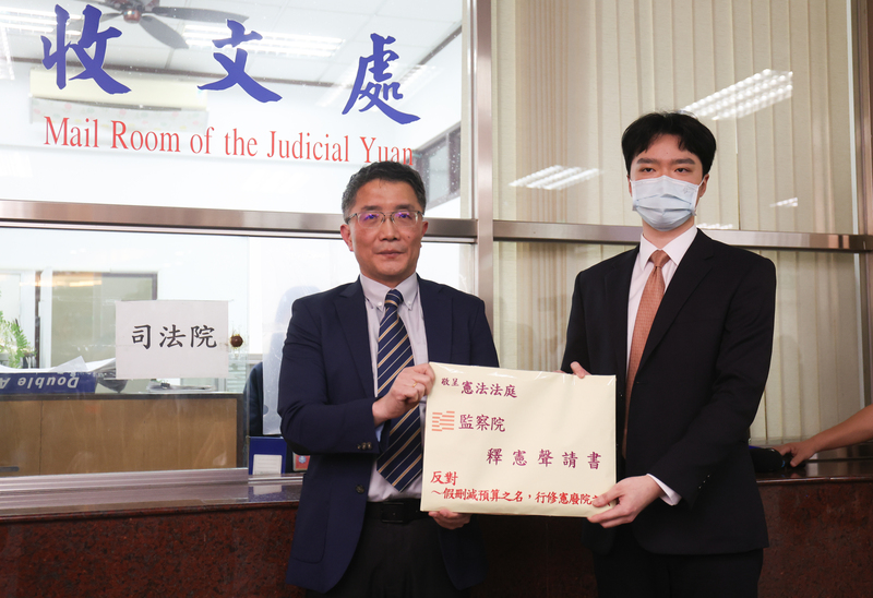 監察院監察調查處長楊昌憲（左）24日下午在律師王首雁（右）陪同下，到憲法法庭遞狀聲請釋憲，牛皮紙袋上標註「反對假刪減預算之名、行修憲廢院之實」文字。(圖：中央社)