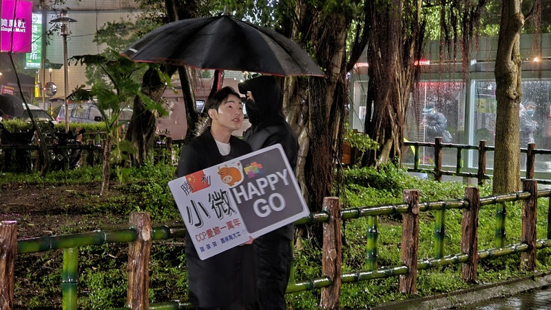 由於小微遲遲未現身機場，網紅八炯（舉牌者）晚間特地到其住處前舉牌送行。(圖：中央社)