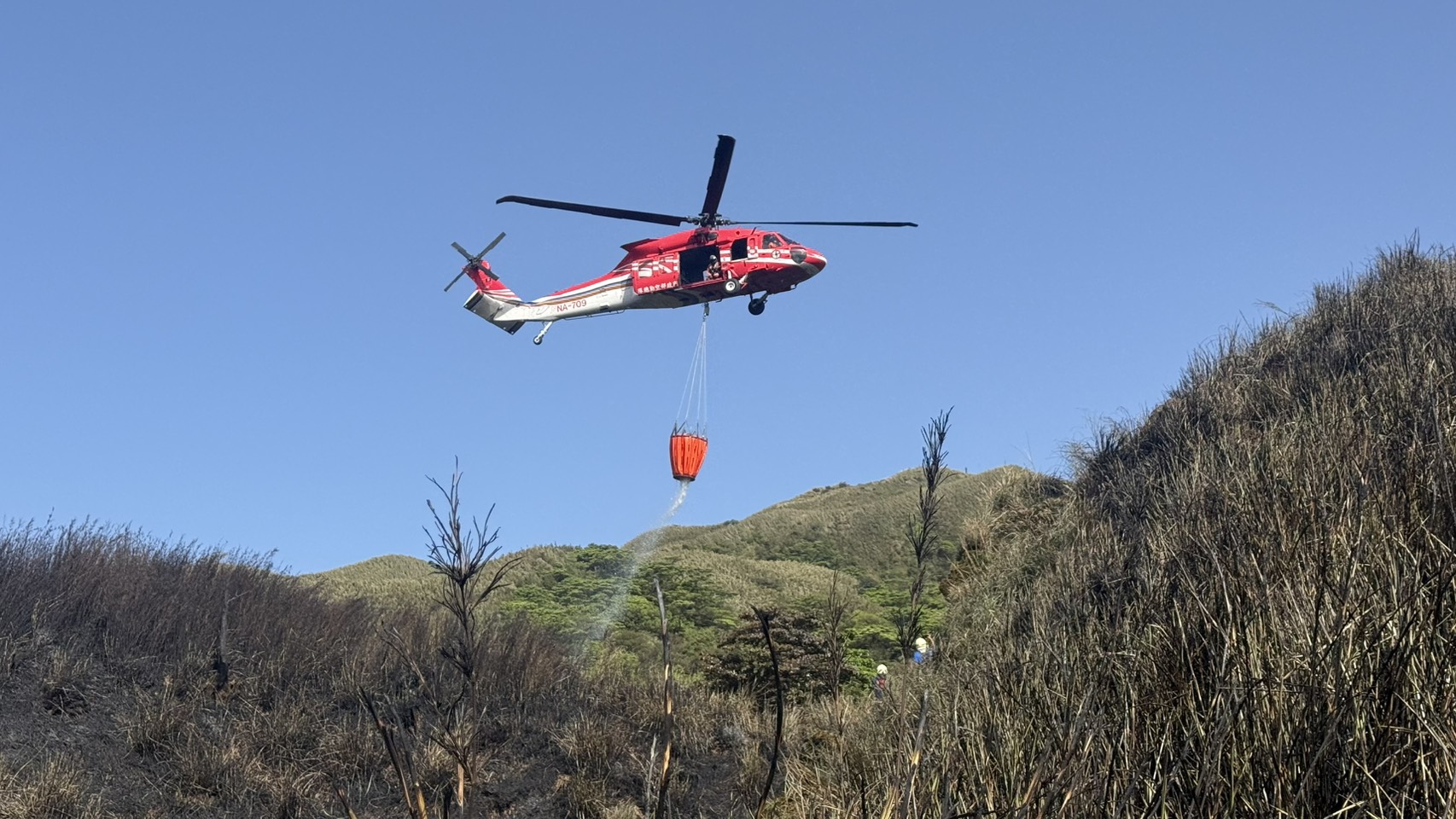 陽明山國家公園小油坑14日上午11時許發生火災，空勤總隊直升機從社子島島頭公園附近的淡水河流域取水後飛到現場灑水滅火。(臺北市政府消防局提供)
