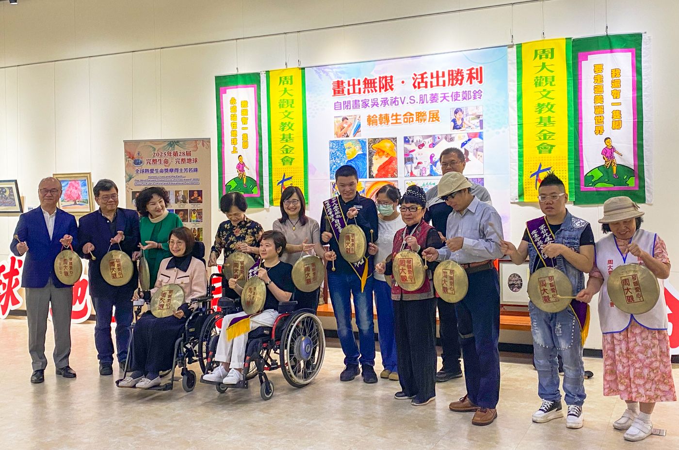 周大觀文教基金會17日頒發全球熱愛生命獎章給畫家吳承祐以及繪本作家鄭鈴，在場貴賓與兩位得主一同敲鑼，為聯合畫展開幕並合影留念。(陳念宜 攝)