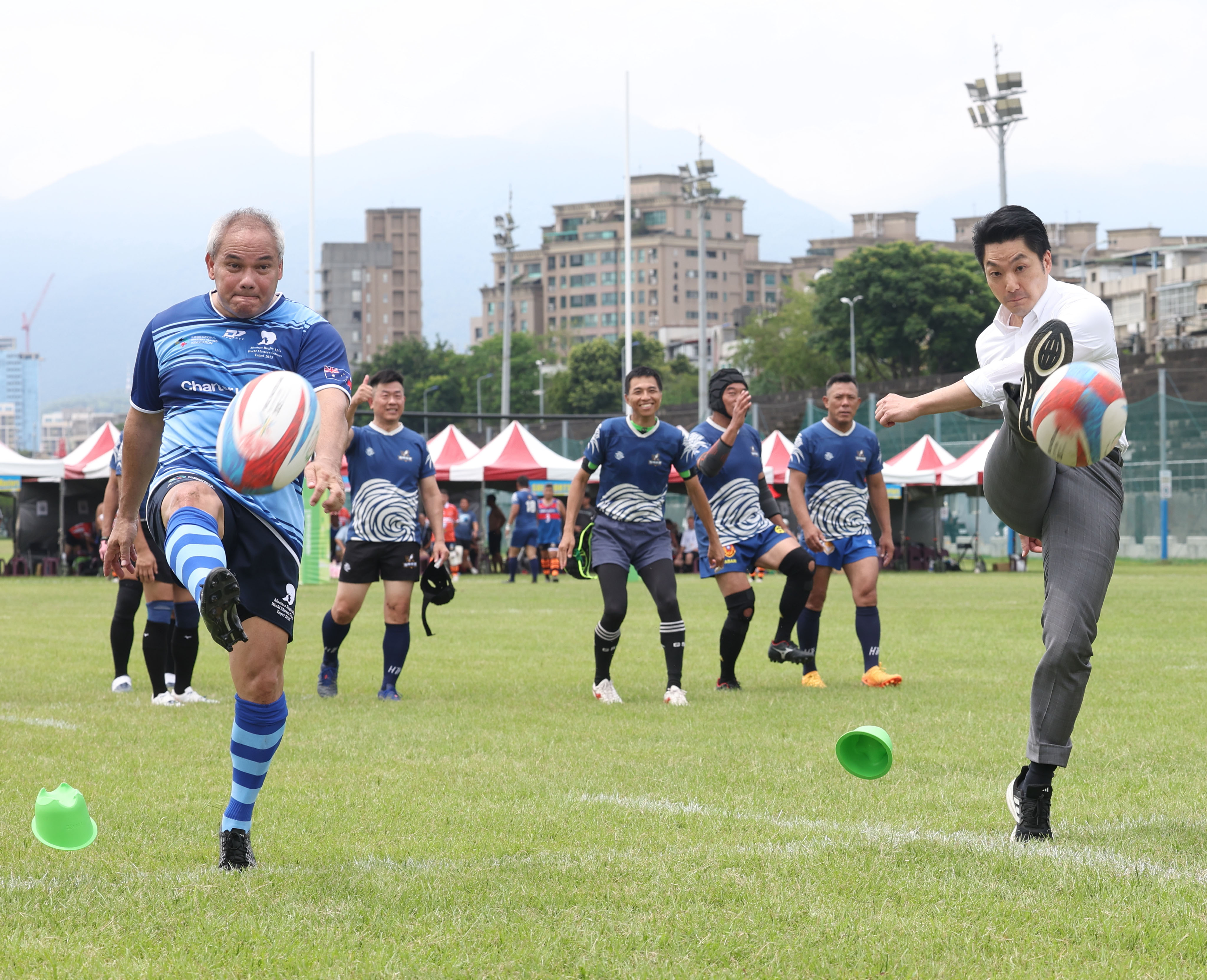 澳洲黃金海岸市長Tom Tate(左)組成澳洲隊「Mosman Masters」，19日參戰世壯運15人制橄欖球賽50歲以上組，台北市長蔣萬安(右)特地前往開球，留下兩人同時開踢的有趣畫面。(世壯運執委會提供 )