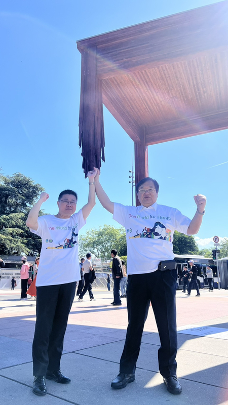 衛生福利部長邱泰源（右）與次長呂建德在世衛總部前廣場，象徵性撐起「三腳椅」塑像缺損的第4支腳，這個故事啟發貝里斯衛福部長柏納在世衛大會比喻「唯有納入台灣，這把椅子才能變得完整」。（衛福部提供） (圖：中央社)